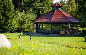SoleAerium, © Stadtgemeinde Mank A pavilion with a red roof in a green park, surrounded by trees and flowers.
