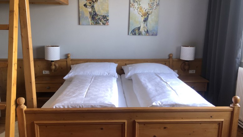 Room example vacation at the Jauerling, © Romana Wiener Cozy bedroom with wooden furniture, double bed, two deer paintings on the wall and a ladder to a loft bed.