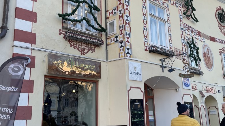 Cafe Allegro, © Wiener Alpen/ Lechner Exterior view of Cafe Allegro with decorated façade and two people in conversation.