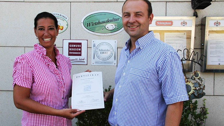 smostlandl, © Leopold Rank Two people holding a certificate in front of a wall of awards.