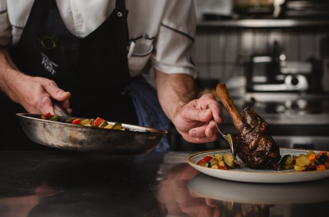 Landlord offers cooking courses, © Niederösterreich Werbung/Daniela Führer A chef in a professional kitchen prepares a dish with meat and vegetables on a plate.
