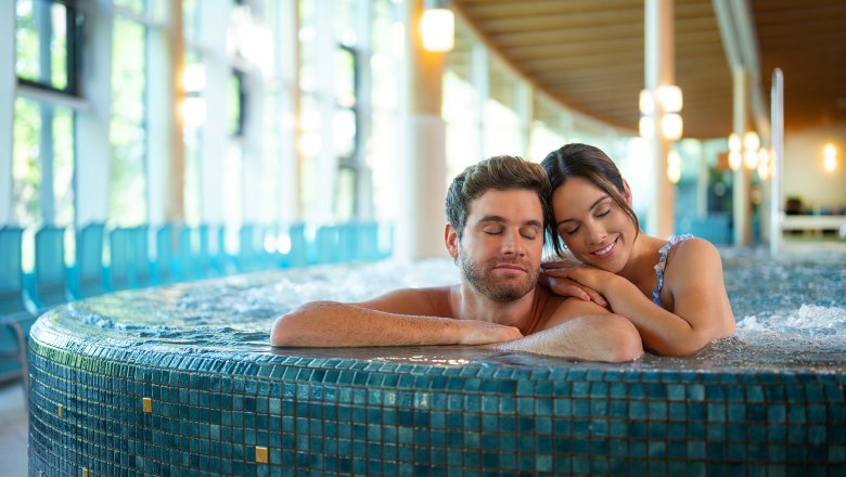 Brine rock world, © Sole Felsen Welt A couple relaxes in a whirlpool in a modern spa with large windows.