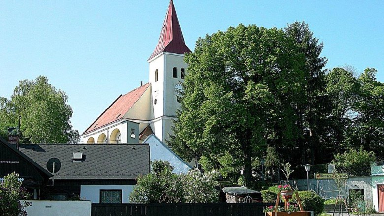 Church, © Gemeinde Hauskirchen A church with a red roof and tower, surrounded by trees and houses.