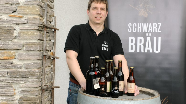 Black brew, © Gerald Schwarz A man stands behind a wooden barrel with bottles of Schwarzbräu beer.