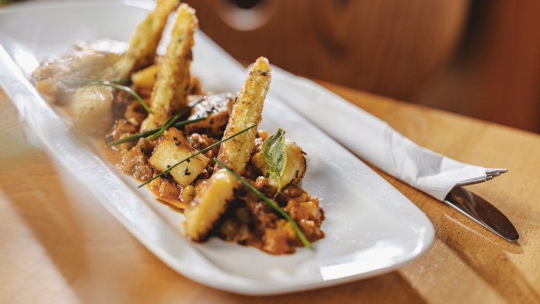This is where pub classics meet gourmet menus, © Niederösterreich Werbung/Michael Reidinger Gourmet dish on a white plate with deep-fried vegetable sticks and herbs.