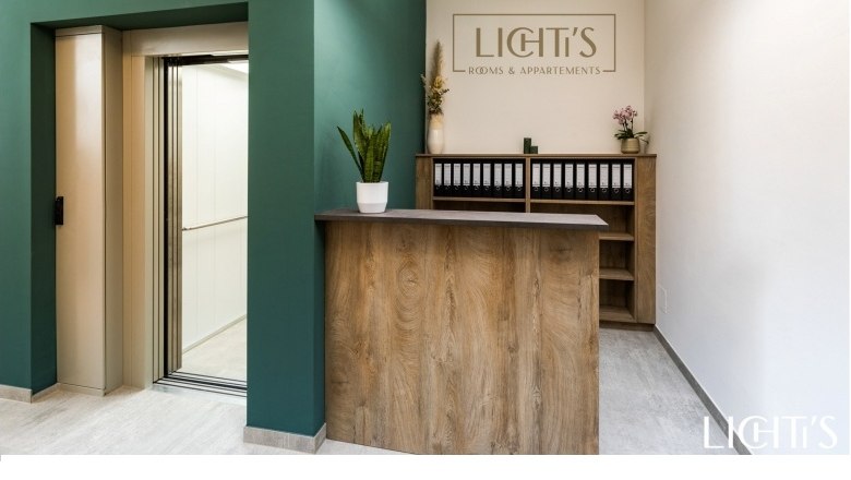 Reception area, © Lichti´s Appartements-Christian Kremsl Reception area with wooden counter, green wall area and elevator.