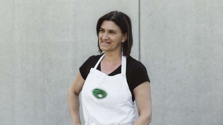 Elisabeth Grötzl, © Niederösterreich Werbung/David Schreiber Woman in a white apron in front of a gray wall.