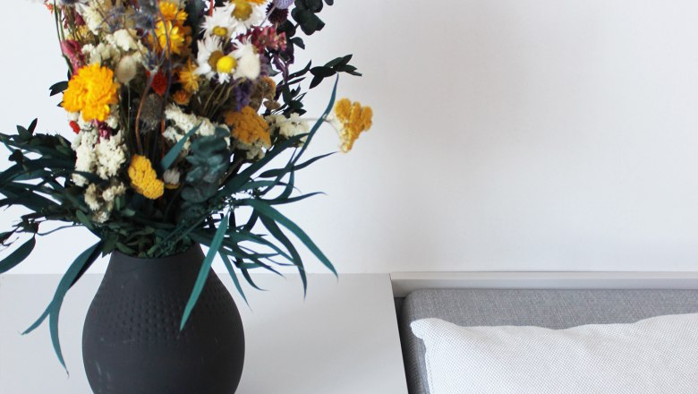 Guest room, © Stadthotel Hollabrunn A table with a black vase full of colorful flowers, a blue magazine with the inscription 'HOLLA!' and a white cushion.