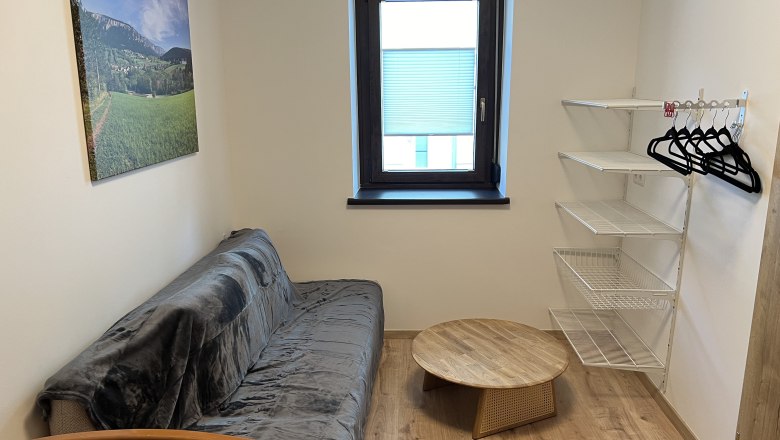 Room, © Anton Sommer Small room with sofa, round wooden table, wall shelf and window.
