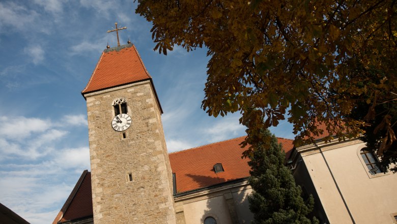 Church Weißenkirchen, © dphoto.at Church tower of Weißenkirchen church with clock and red roof, surrounded by autumn leaves and blue sky.