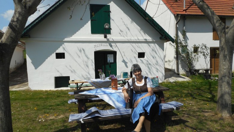 Wine cellar lane Sierndorf/March, © Franz Rauscher A woman in traditional dress sits on a bench in front of a white building with green shutters.
