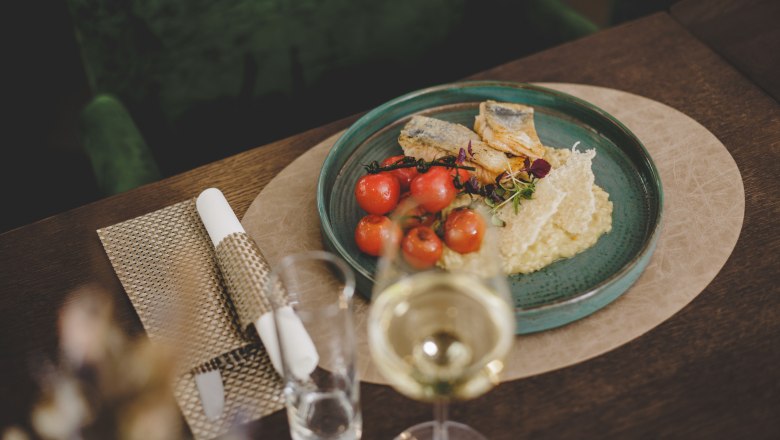 Grilled sea bream fillet with lemon risotto, © Niederösterreich-Werbung/David Schreiber A plate of grilled gilthead bream fillet, lemon risotto and cherry tomatoes, served on a wooden table with a glass of white wine.