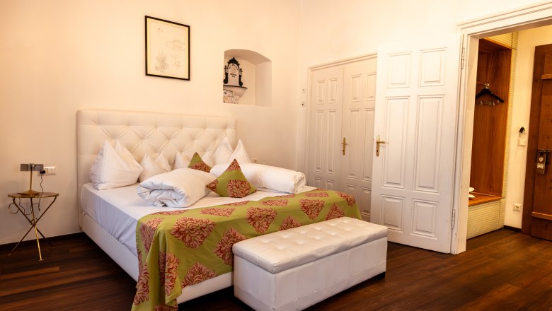 Hotel Landhaus Moserhof, © Niederösterreich Werbung / Maximilian Pawlikowsky Elegant hotel room with large bed, white furniture and wooden floor.