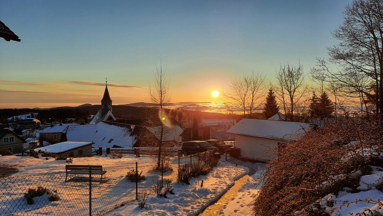 Sunrise from the Belle Air Logde in winter, © Christoph Gierlinger Winter sunrise over a snowy landscape with a church and houses.