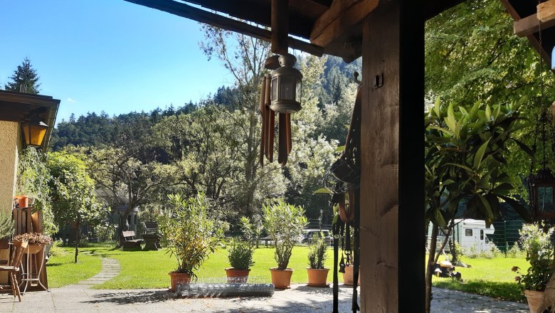 Inner courtyard, © Familie Kellner A sunny courtyard with lawn, trees and potted plants. In the foreground, a covered terrace with a lantern and garden furniture.