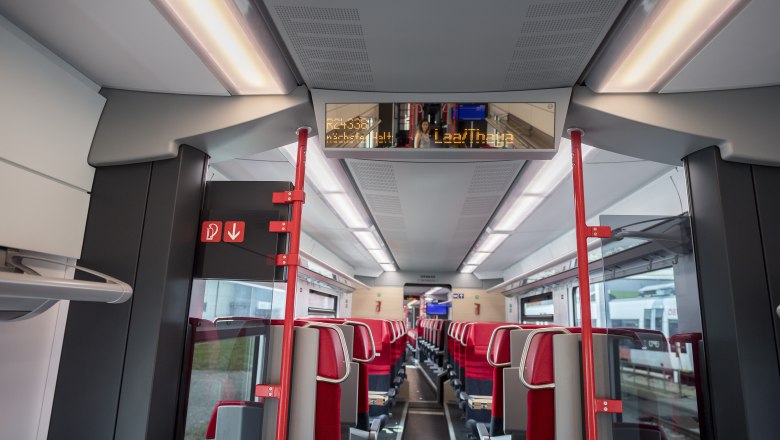 Train, © Weinviertel Tourismus GmbH / Herbst Interior view of a modern train compartment with red seats and digital display board.