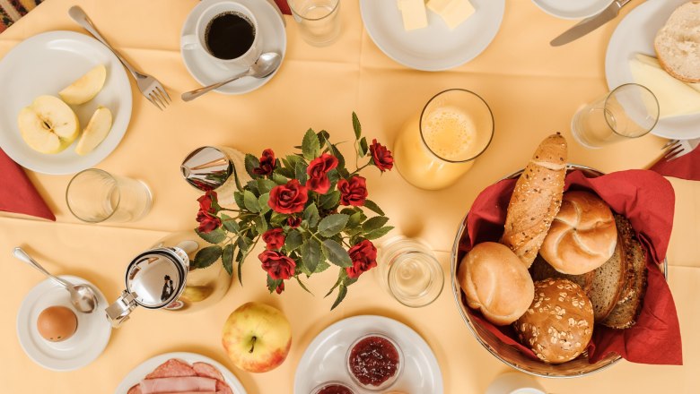 Breakfast, © Rita Newman A laid breakfast table with bread rolls, cold cuts, jam, coffee, orange juice and a bouquet of flowers in the middle.