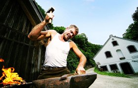 Eybl Ybbsitz hammer mill, © weinfranz.at A blacksmith works with a hammer on an anvil in front of an outdoor building.