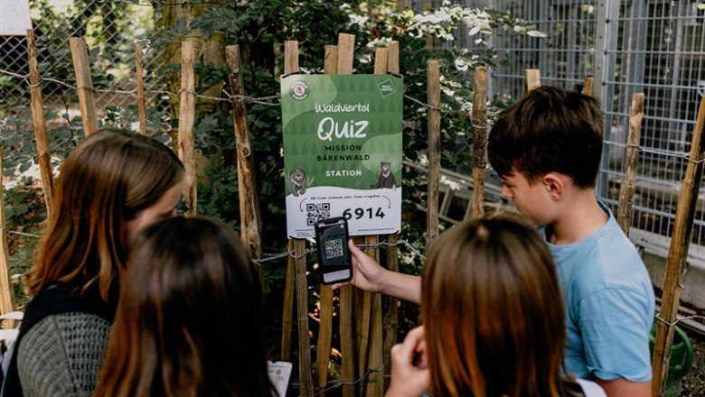Arbesbach Bear Sanctuary, © Waldviertel Tourismus, Matthias Streibel Children stand in front of a sign with the words 'Waldviertel Quiz Mission Bärenwald Station' and scan a QR code with a smartphone.
