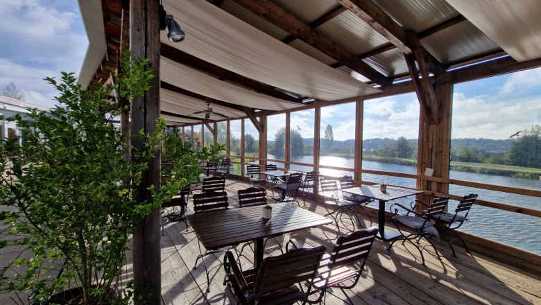 Terrace, © Die Käsemacherwelt Covered terrace with wooden tables and chairs by the water.