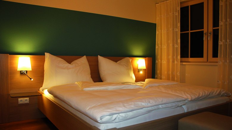 Guest room, © Widhalm A cozy guest room with a double bed, two bedside lamps and a window with curtains.