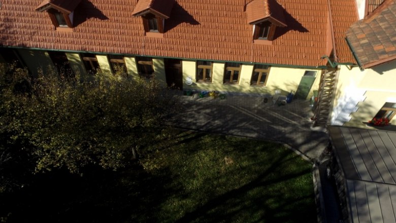 The vacation apartments from above, © dmgrauszer Aerial view of a building with a red tiled roof and several windows, surrounded by a garden.