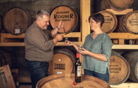 Tasting, © Christoph Kerschbaum Two people at a tasting in a distillery with wooden barrels in the background.
