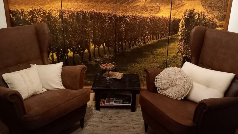 Cozy corner, © Familie Fleischmann Two brown armchairs with cushions in front of a wall with a landscape photo wallpaper of a vineyard.