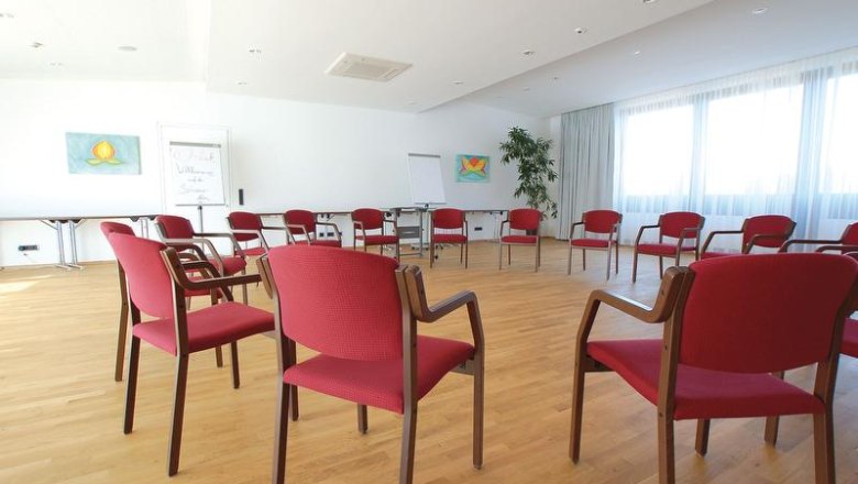 Seminar room, © Hotel Schwarz Alm A bright seminar room with red chairs in a circle, a wooden floor and large windows.