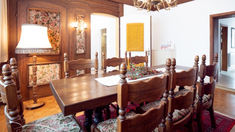 Lounge and dining room, © Doris Eminger Rustic dining room with wooden furniture, chandelier and floral patterns.