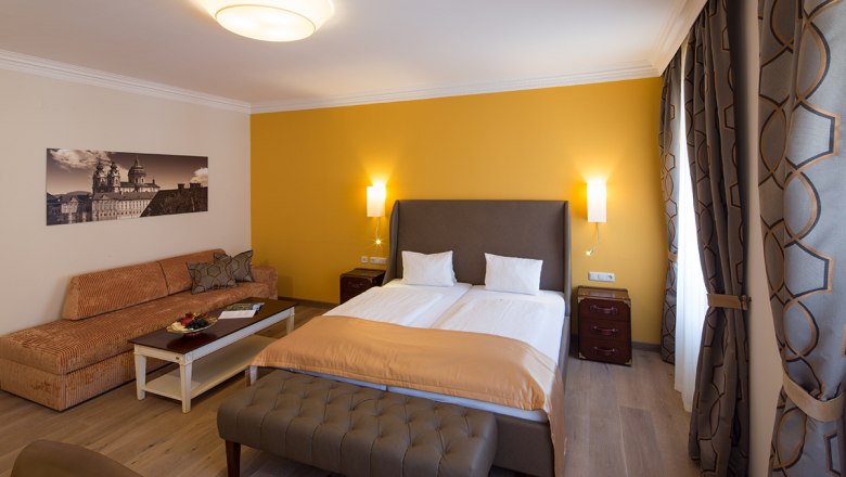 Room example in the Hotel-Restaurant Zur Post, © Lachlan Blair Hotel room with double bed, yellow wall, sofa, table and curtains.