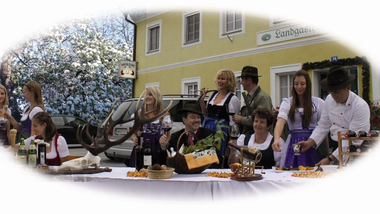 Winklehner country inn, © Landgasthof Winklehner People in traditional costume celebrate in front of a country inn with food and drink.