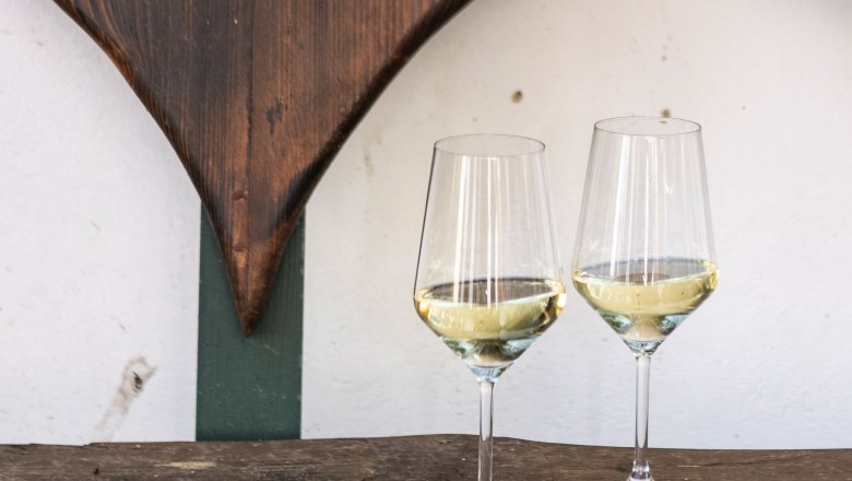 Wine glasses, © Weinviertel Tourismus / Doris Schwarz-König Two wine glasses with white wine on a wooden table in front of a wooden heart decoration.
