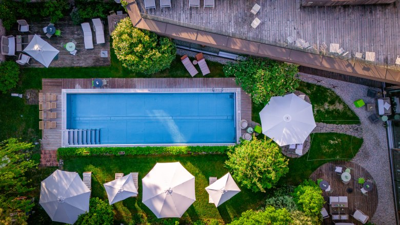 Hotel Landhaus Moserhof, © Niederösterreich Werbung / Maximilian Pawlikowsky Aerial view of a pool with surrounding sun loungers and parasols in a garden.