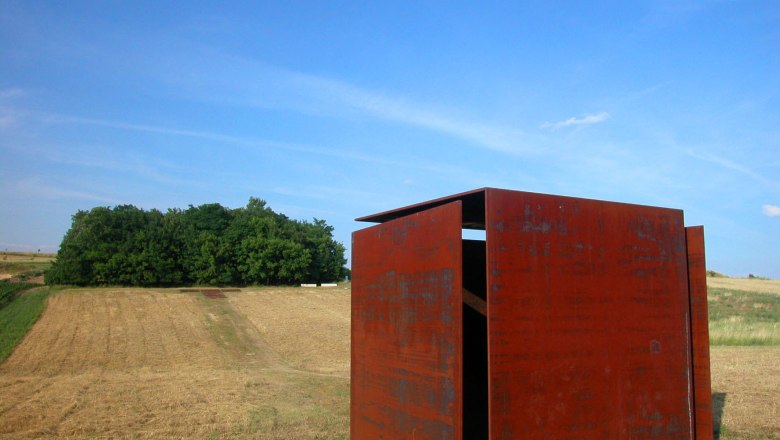 Wind cube house, © StadtGemeinde Mistelbach Rusty metal cube on a field with trees in the background.