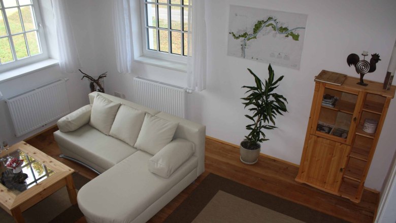 Sitting area in the vacation apartment at the Schmidl organic winery, © Weingut Schmidl Cozy sitting area with beige sofa, wooden table, plant and shelf in a vacation apartment.