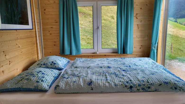 Bed 160 x 200 cm, © Villa to go Wooden interior with bed, window and blue curtains.