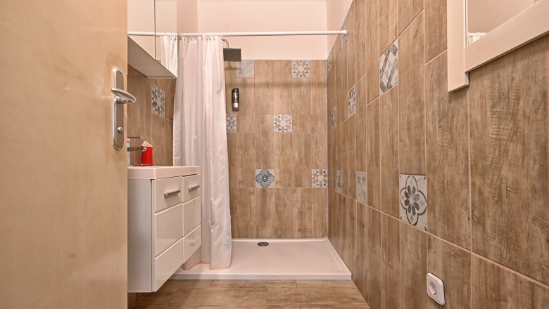 Bathroom, © Christine Kuppelwieser Modern bathroom with shower cubicle, tiled walls and washbasin.