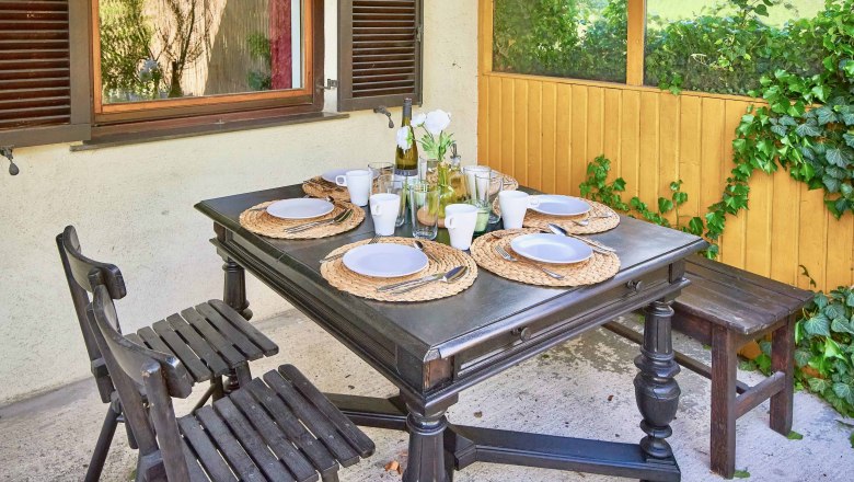 Top 1 - Terrace, © VP FeWo OG Set table on a terrace with four seats, wooden furniture and plants in the background.