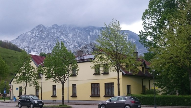Exterior view, © Gudrun Rath Yellow house in front of a snow-covered mountain and cloudy sky.