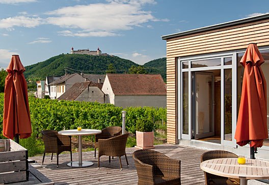 Terrace with Göttweig Abbey, © Weinresidenz Sonnleitner Terrace with tables, chairs and red parasols, Göttweig Abbey on a hill in the background.