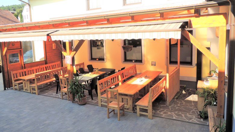 The guest garden of Gasthaus Posch, © Karl Gradwohl A cozy guest garden with wooden benches and tables under an awning.