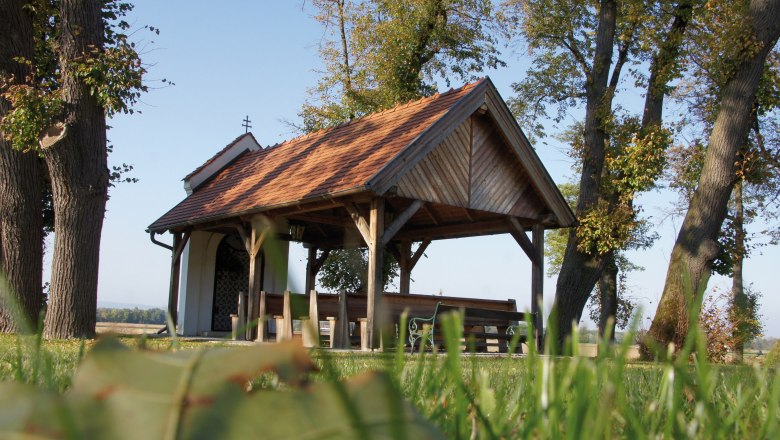 Walpersbach, © Thermengemeinden Small chapel with wooden roof and benches, surrounded by trees and meadow.