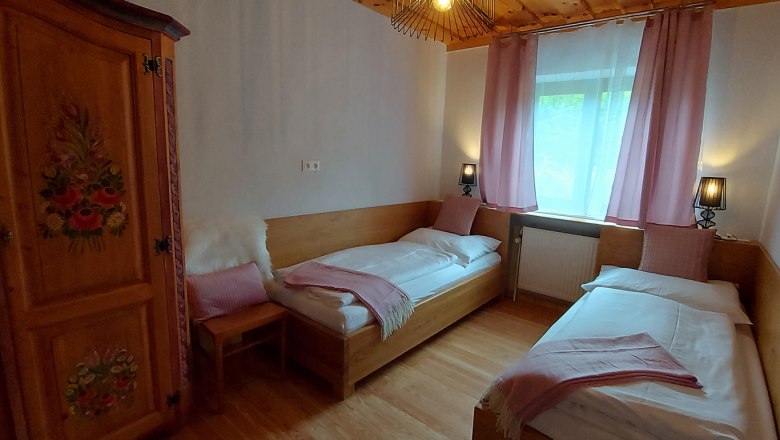 Double room on the ground floor, © Bernadette Gierlinger Cozy bedroom with two single beds, wooden furniture and pink curtains.