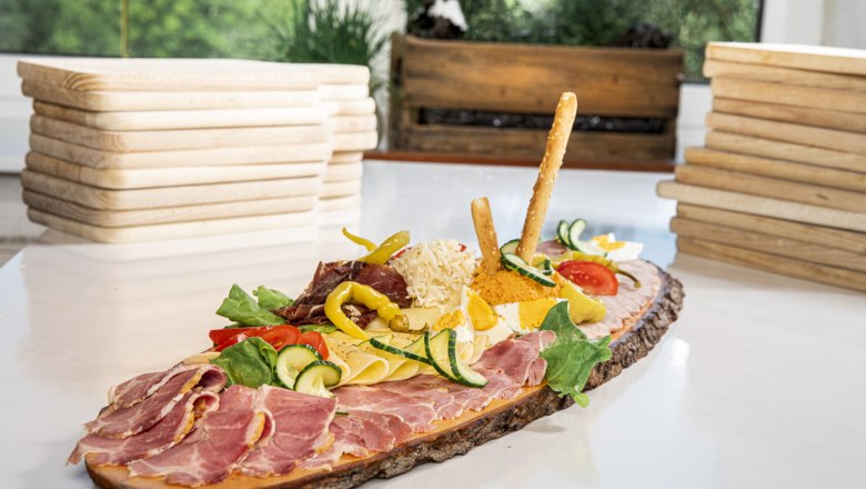 Heurigen platter, © Nimo Zimmerhackl A Heurigen platter with ham, cheese, vegetables and breadsticks on a rustic wooden board.