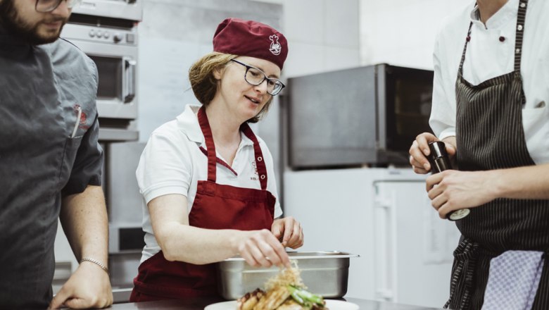 Landlady and cook Ingrid Schöner, © Niederösterreich Werbung/David Schreiber Three chefs in a restaurant kitchen prepare a dish.