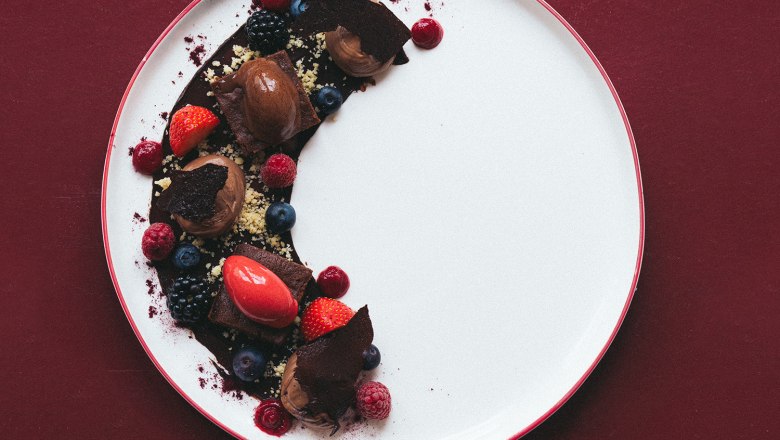 Chocolate mousse with berries, © Hofmeisterei Hirtzberger/Julius Hirtzberger A dessert plate with chocolate mousse, berries and chocolate pieces on a red background.
