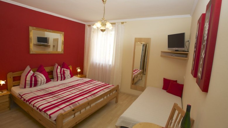 Room example, © Familie Ebner Cozy room with double bed, single bed, red accent wall and TV.