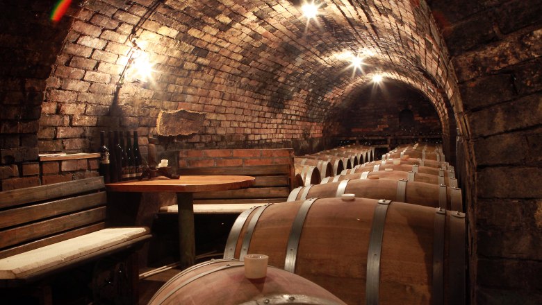 Wine cellar at the Fink Winery, © weinfranz.at A wine cellar with wooden barrels and a table with benches.