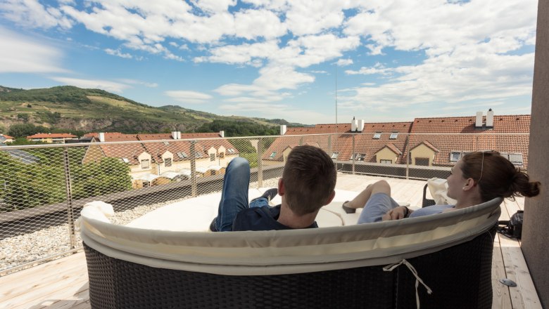 Wine lodge terrace with stunning views, © KASTNER NEW MEDIA - kastner.tv Two people relax on a terrace with a view of rooftops and hills.